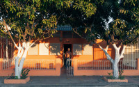 Orange house with big trees in front, white shutters. Evening light, man standing at the doorway.